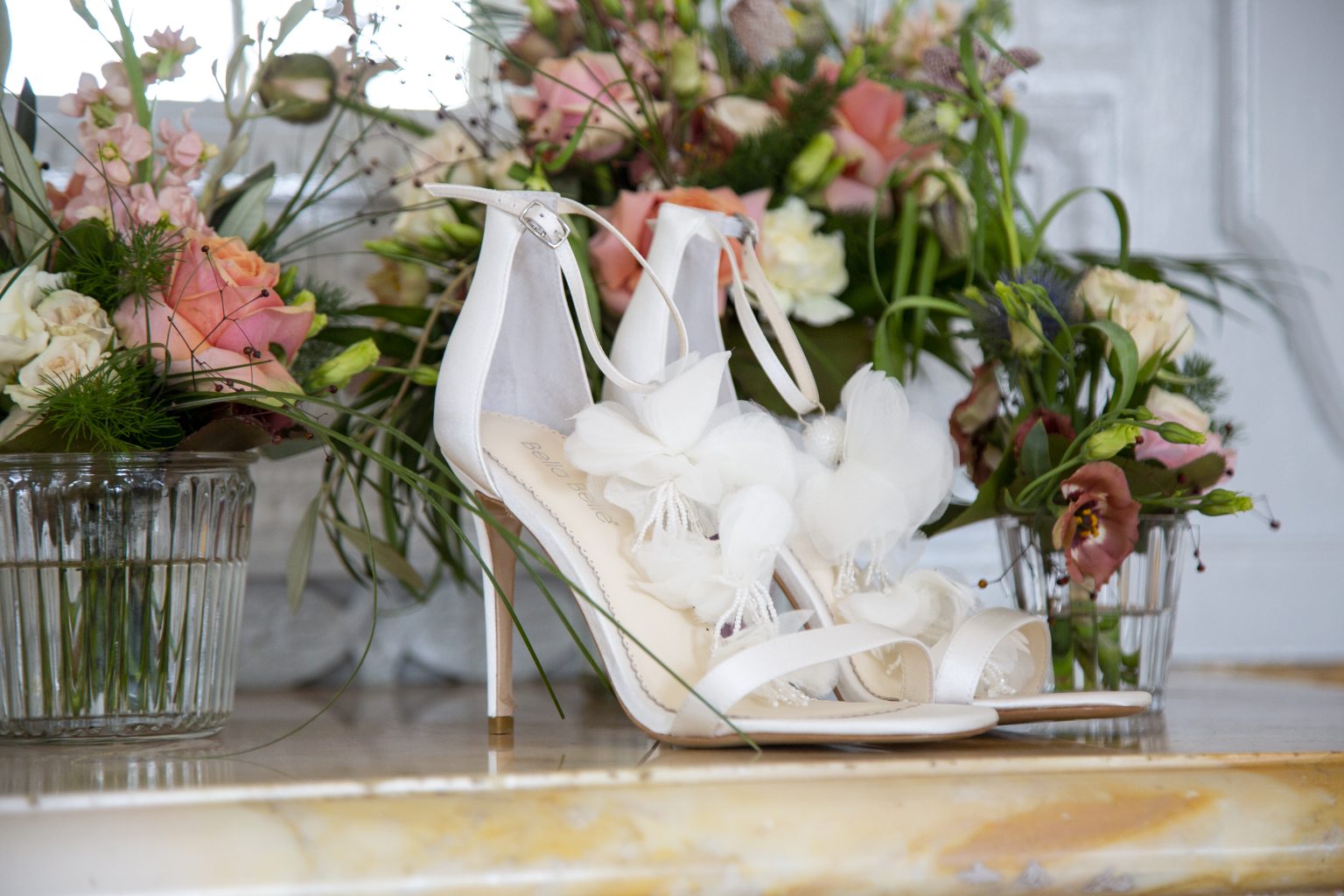 Hochzeitsfoto von Sarah Seiler Fotografie Brautschuhe liegen dekorativ vor einem Blumenarrangement und Sarah Seiler Fotografie fotografiert dieses Detail.