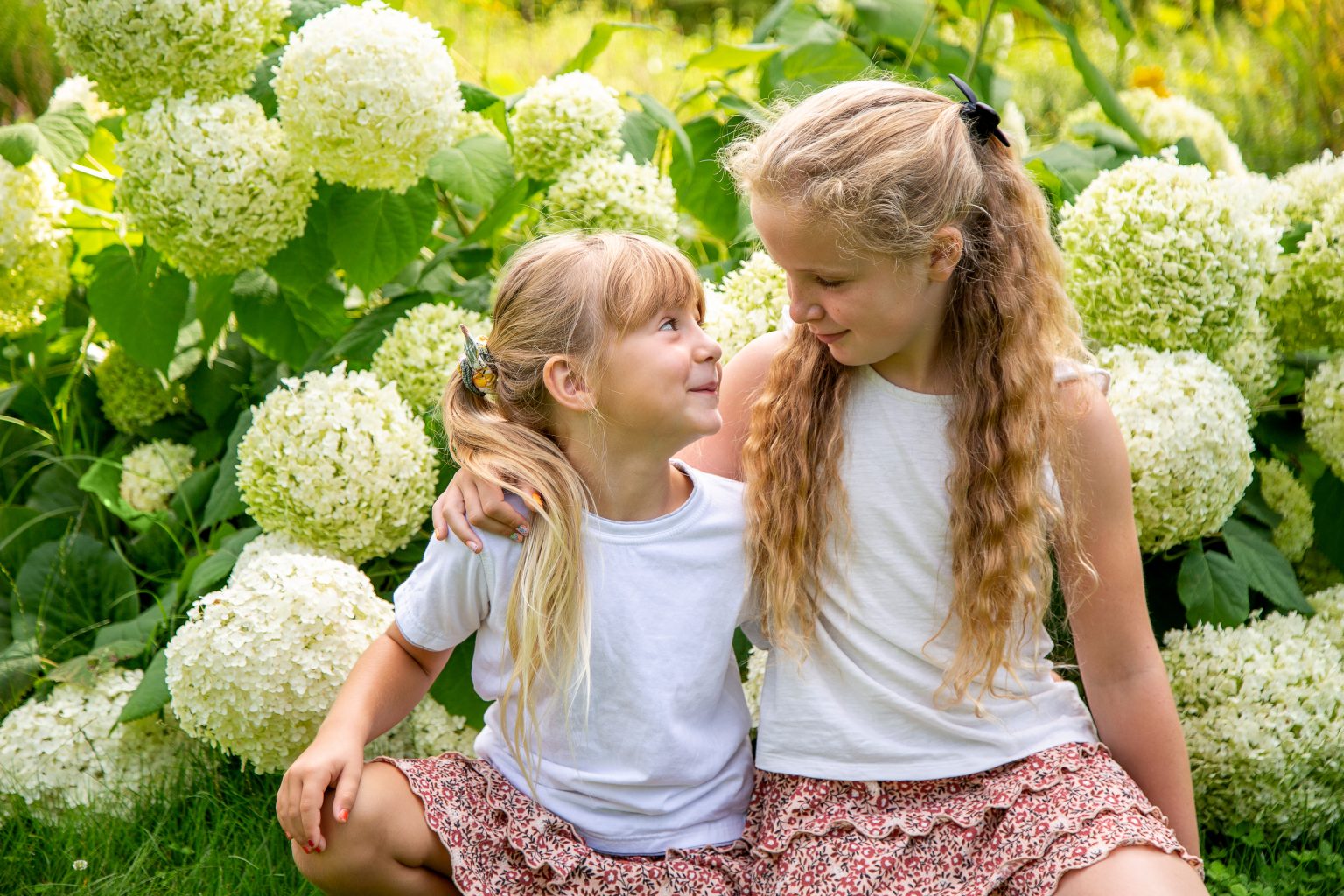Familienfoto von Sarah Seiler Fotografie Zwei Mädchen sitzen nebeneinander und Sarah Seiler Fotografie hält den Moment fest.