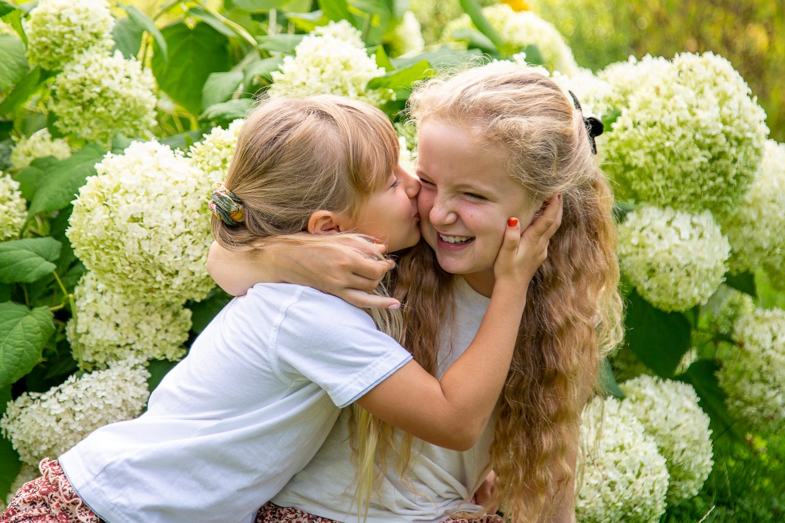 Familienfoto von Sarah Seiler Fotografie Zwei Mädchen umarmen sich liebevoll und Sarah Seiler Fotografie fotografiert sie.