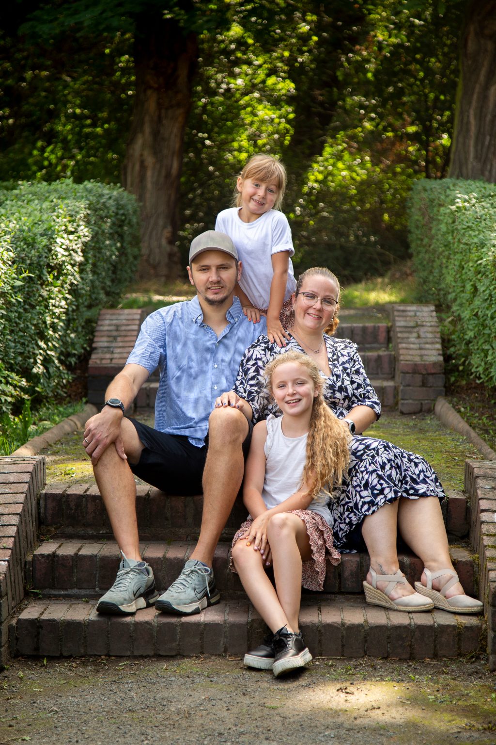 Familienfoto von Sarah Seiler Fotografie Eine Familie sitzt zusammen auf einer Parktreppe und Sarah Seiler Fotografie hält diesen Moment fest.
