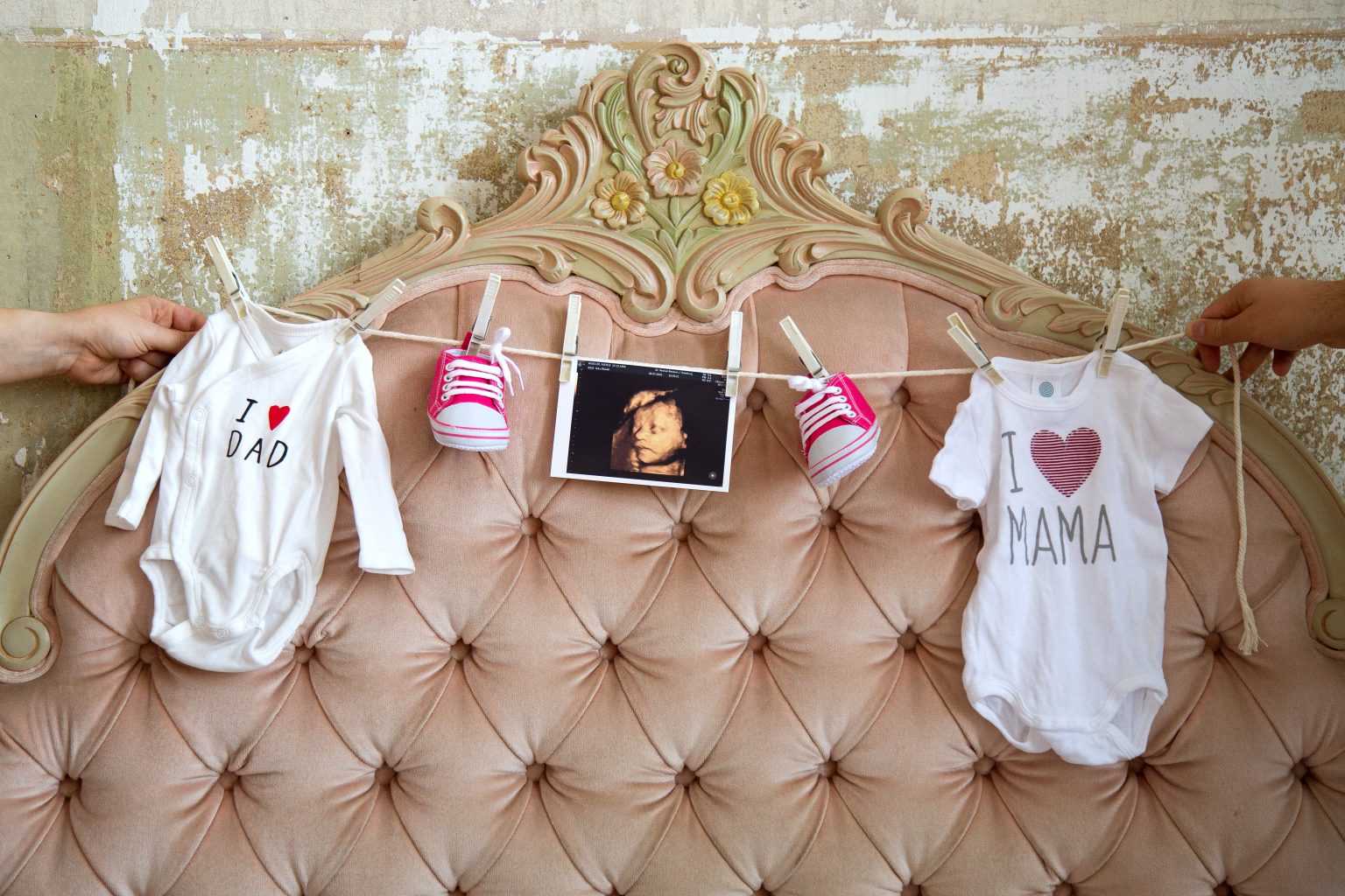 Baby Ankündigung – Sarah Seiler Fotografie Babyartikel hängen dekorativ am Bettgestell und Sarah Seiler Fotografie fotografiert sie.