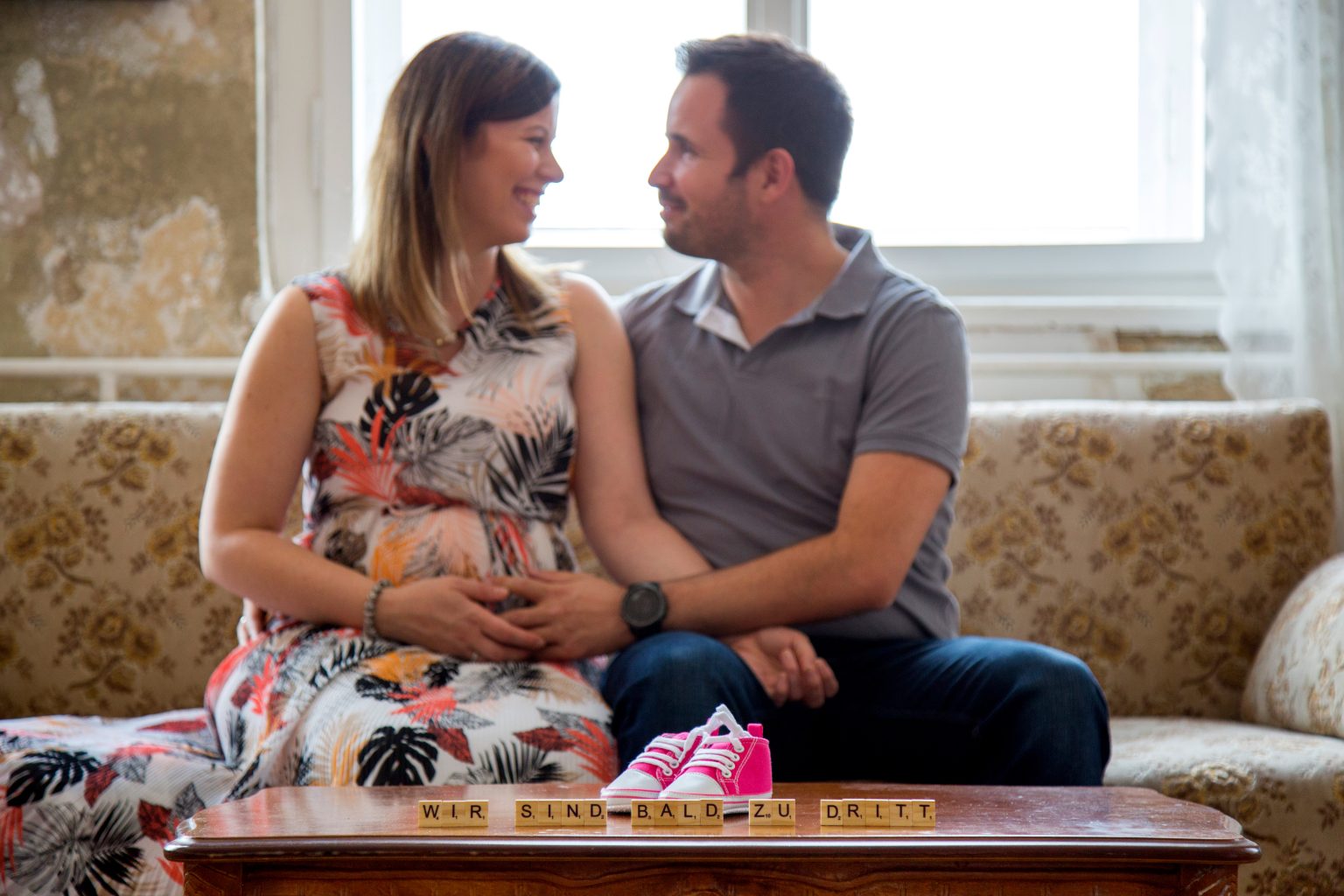 Familienfoto von Sarah Seiler Fotografie Ein Paar sitzt zusammen und hält Babyschuhe, während Sarah Seiler Fotografie dieses Bild aufnimmt.