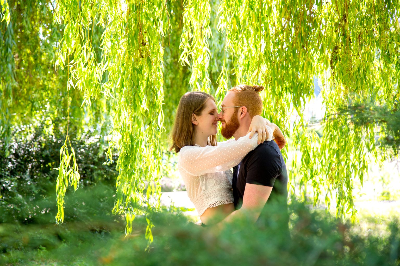 Paarshooting von Sarah Seiler Fotografie Ein Paar umarmt sich unter einer Weide und Sarah Seiler Fotografie fotografiert sie.