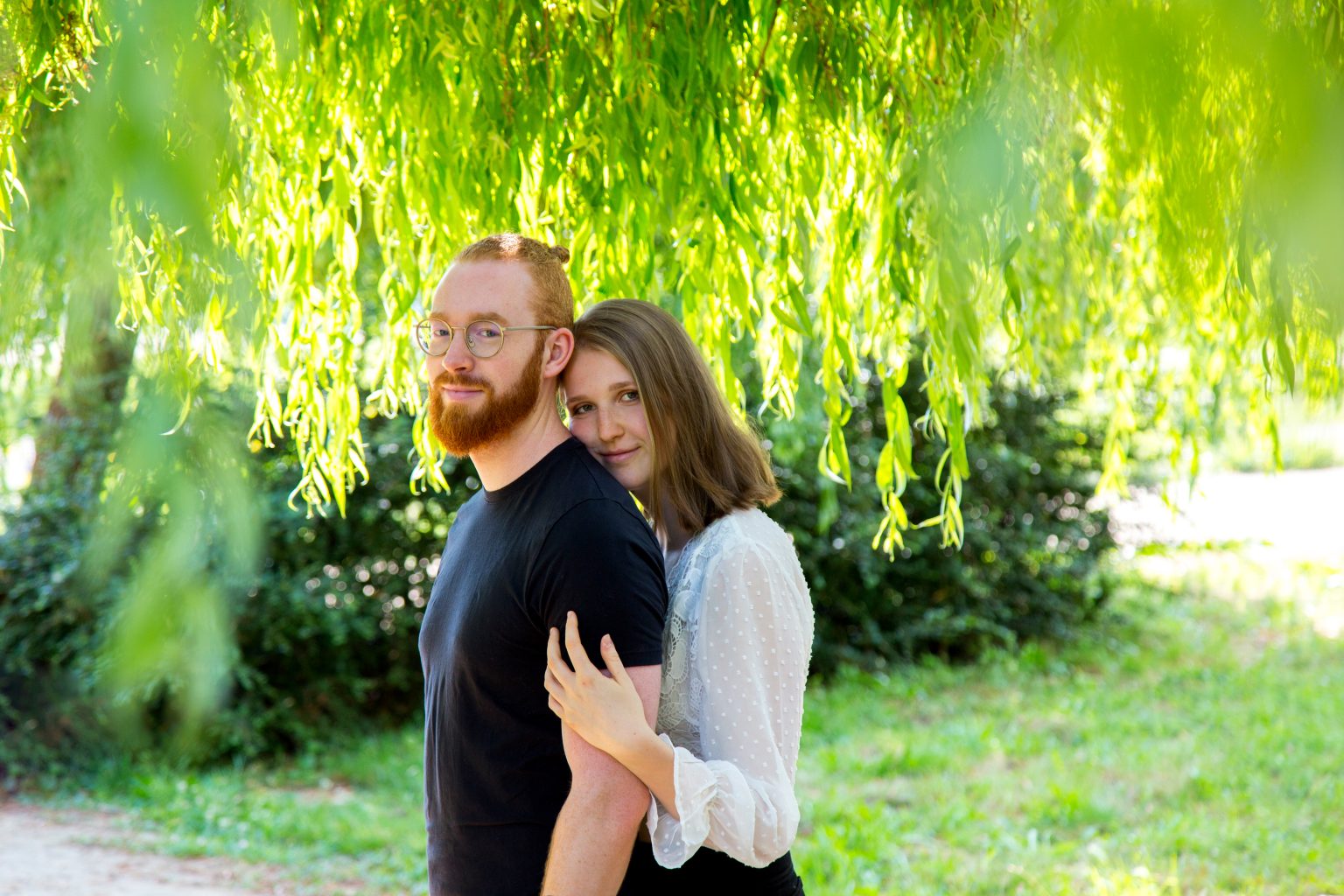 Sarah Seiler Fotografie – Outdoorshooting Ein Paar steht unter einer hängenden Weide und Sarah Seiler Fotografie fotografiert sie.