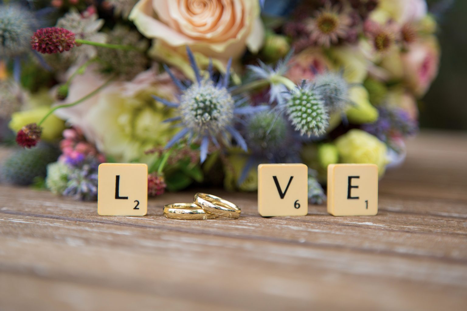 Hochzeitsfoto von Sarah Seiler Fotografie Eheringe liegen dekorativ neben Scrabble Buchstaben und Sarah Seiler Fotografie fotografiert sie.