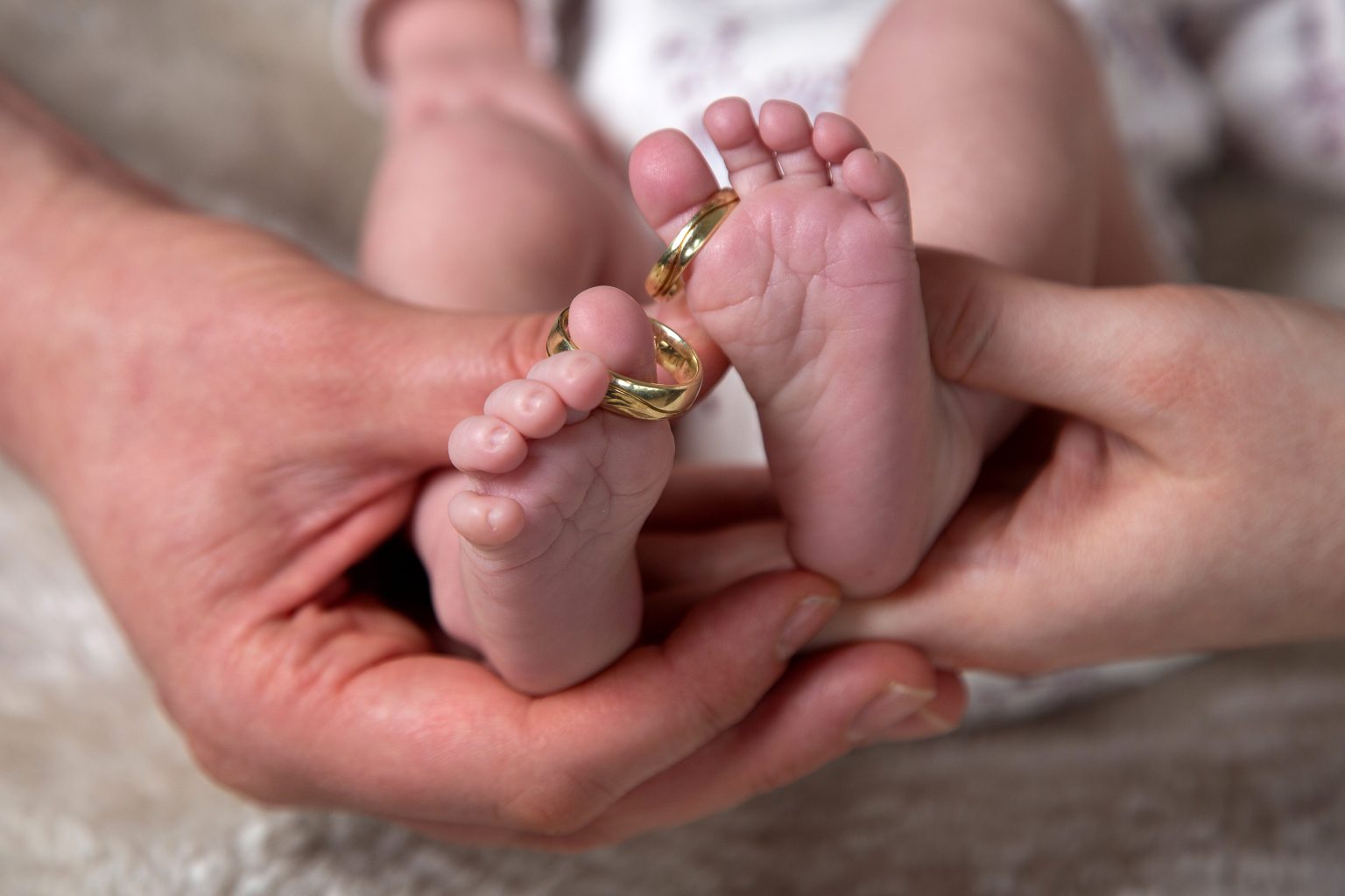 Hochzeitsfoto von Sarah Seiler Fotografie Ein Baby wird auf Händen gehalten und Sarah Seiler Fotografie fotografiert seine Füße mit Eheringen.