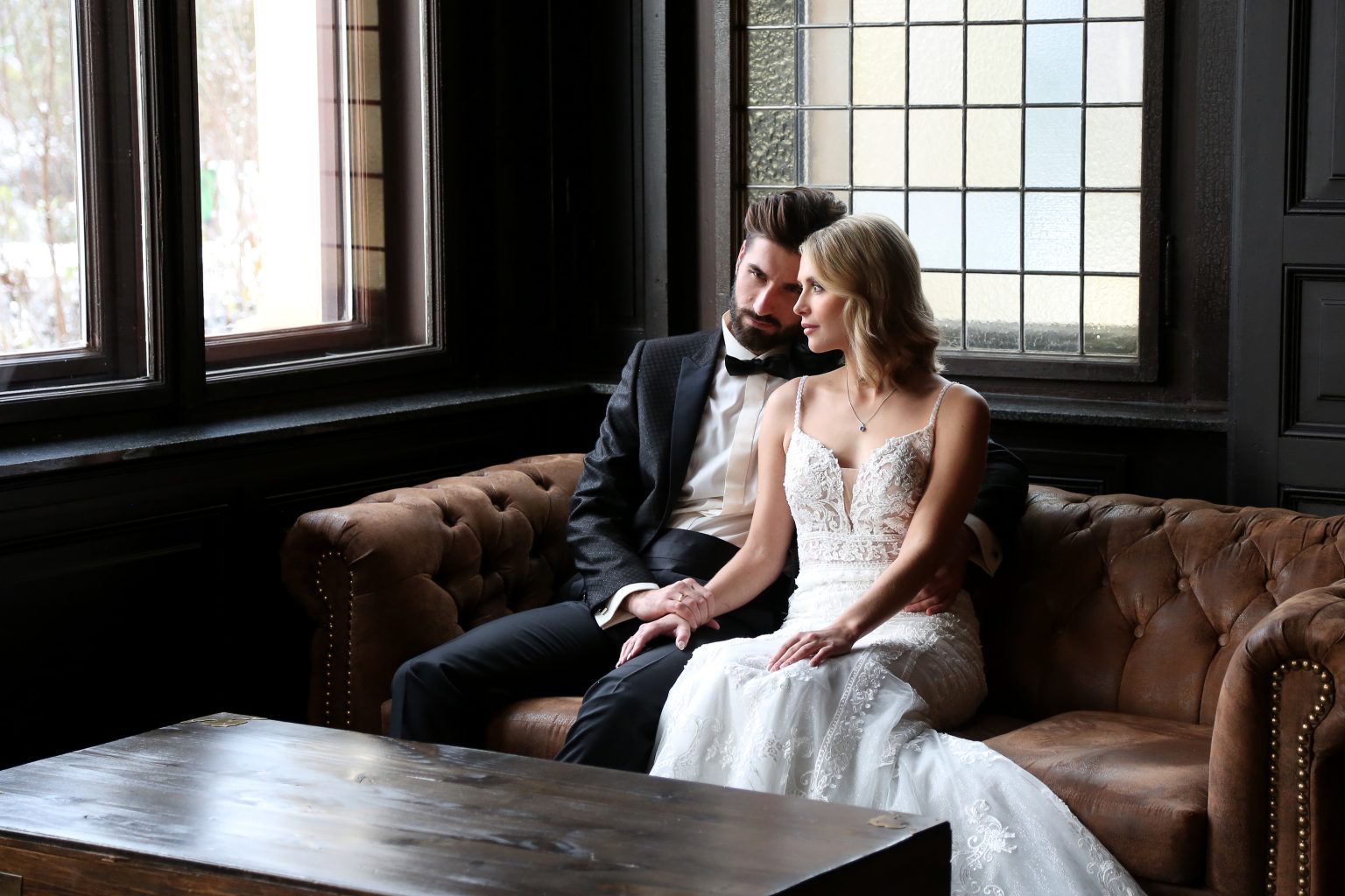 Hochzeitsfoto von Sarah Seiler Fotografie Ein Hochzeitspaar sitzt eng umarmt auf einer Ledercouch in einem historischen Raum und Sarah Seiler Fotografie hält diesen Moment fest.