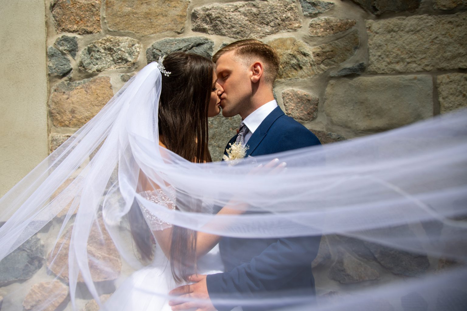 Hochzeitsfoto von Sarah Seiler Fotografie Ein Hochzeitspaar steht eng zusammen und Sarah Seiler Fotografie fotografiert die Bewegung des Schleiers.