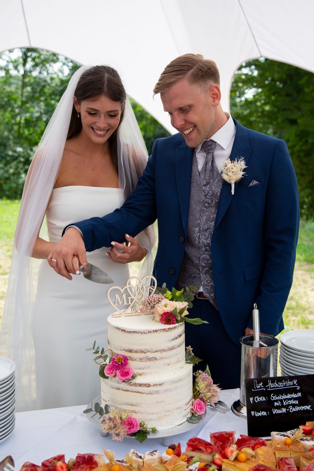 Hochzeitsfoto von Sarah Seiler Fotografie Ein Hochzeitspaar schneidet gemeinsam die Torte und Sarah Seiler Fotografie fotografiert sie.