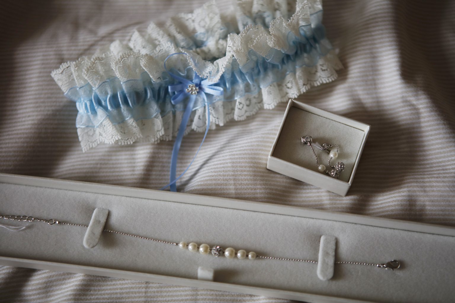 Hochzeitsfoto von Sarah Seiler Fotografie Brautaccessoires wie Strumpfband und Schmuck liegen dekoriert und werden von Sarah Seiler Fotografie fotografiert.