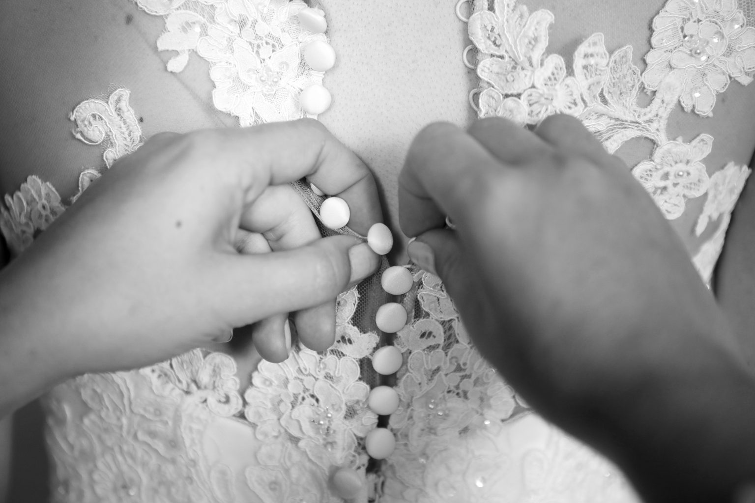 Hochzeitsfoto von Sarah Seiler Fotografie Jemand knöpft das Brautkleid der Braut zu und Sarah Seiler Fotografie hält diesen Moment fest.