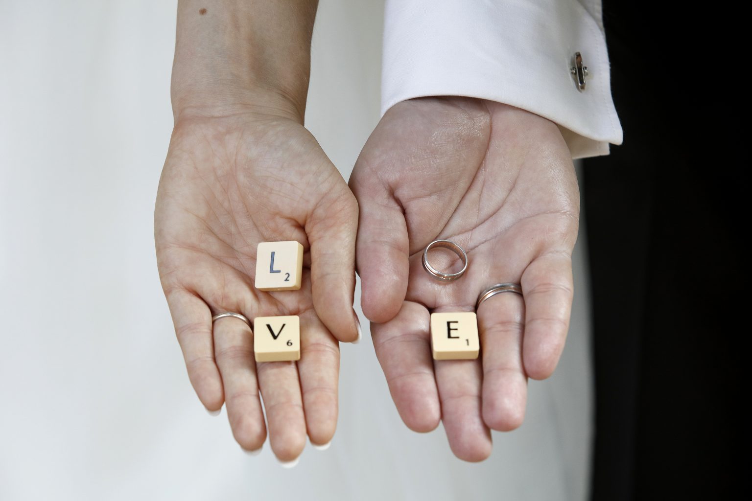 Hochzeitsfoto von Sarah Seiler Fotografie Zwei Hände halten Scrabblebuchstaben und Eheringe, und Sarah Seiler Fotografie fotografiert diesen Moment.