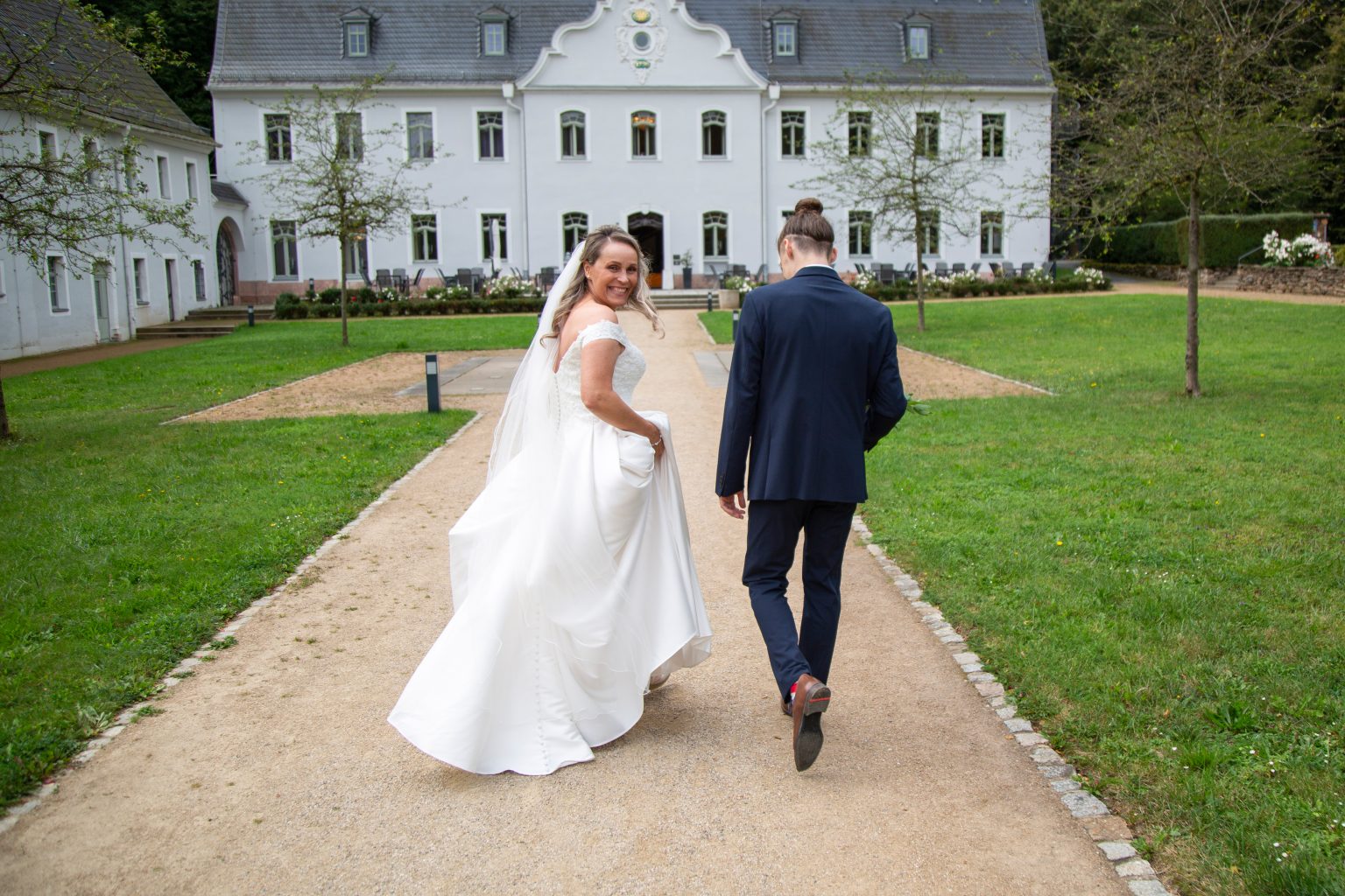 Hochzeitsfoto von Sarah Seiler Fotografie Ein Hochzeitspaar läuft Hand in Hand vor einer Hochzeitslocation und Sarah Seiler Fotografie hält diesen Moment fest.