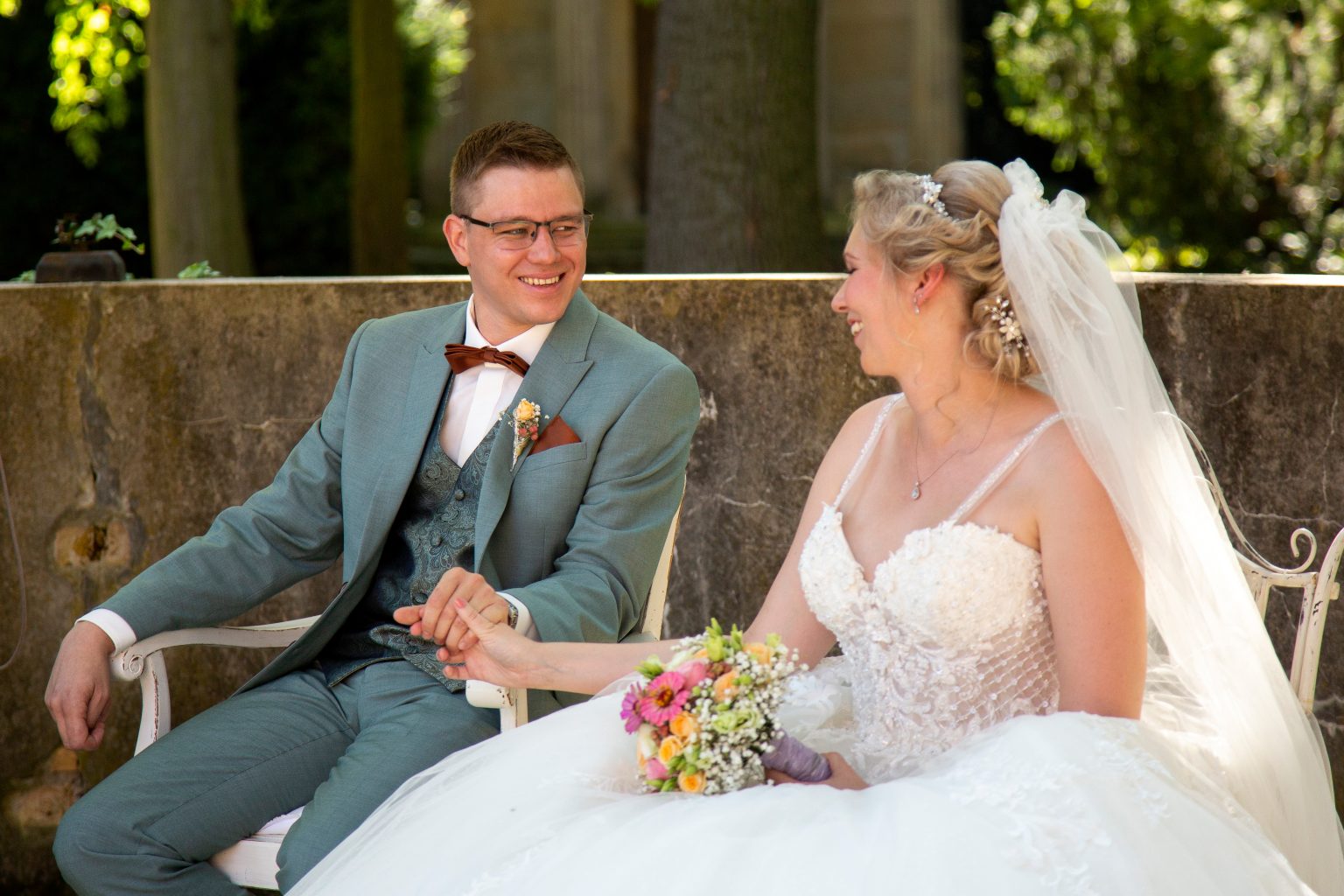 Hochzeitsfoto von Sarah Seiler Fotografie Ein Hochzeitspaar sitzt draußen nebeneinander und Sarah Seiler Fotografie fotografiert sie.