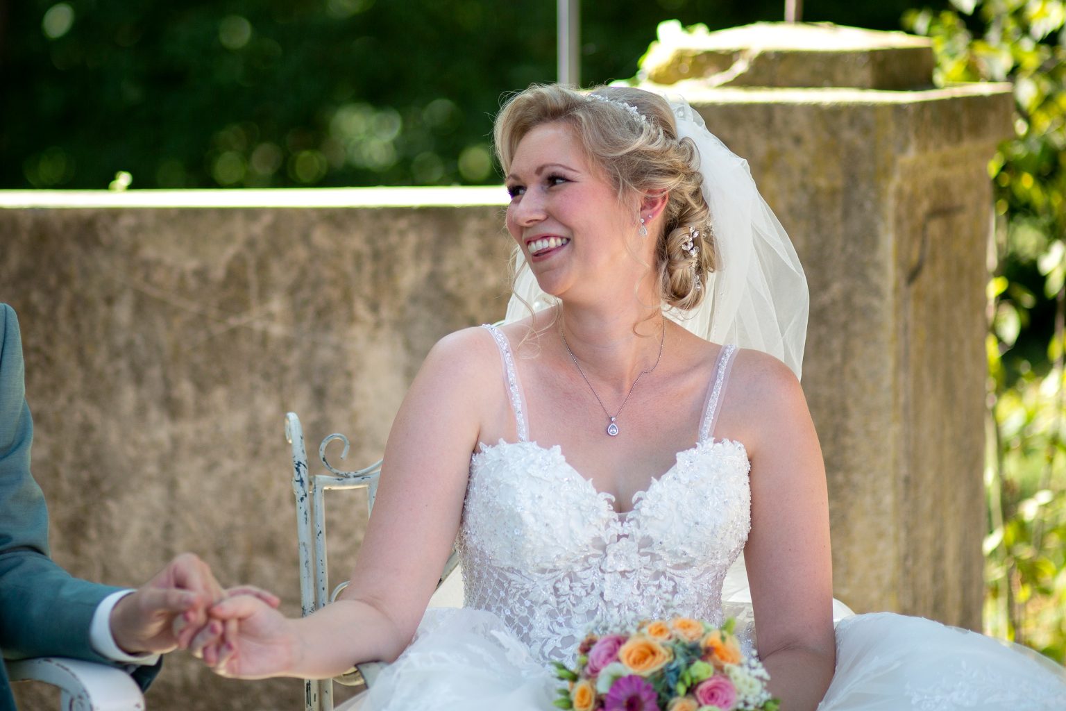 Hochzeit- Sarah Seiler Fotografie Eine Braut sitzt lächelnd auf ihrem Stuhl und Sarah Seiler Fotografie fotografiert sie.