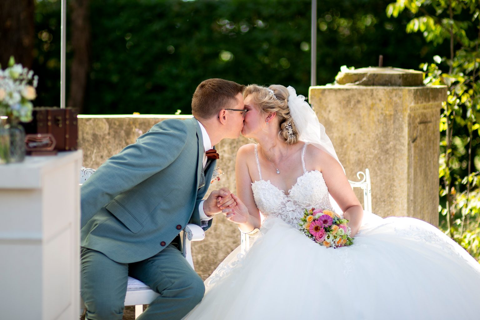 Hochzeitsfoto von Sarah Seiler Fotografie Ein Hochzeitspaar sitzt draußen und küßt sich, während Sarah Seiler Fotografie sie fotografiert.