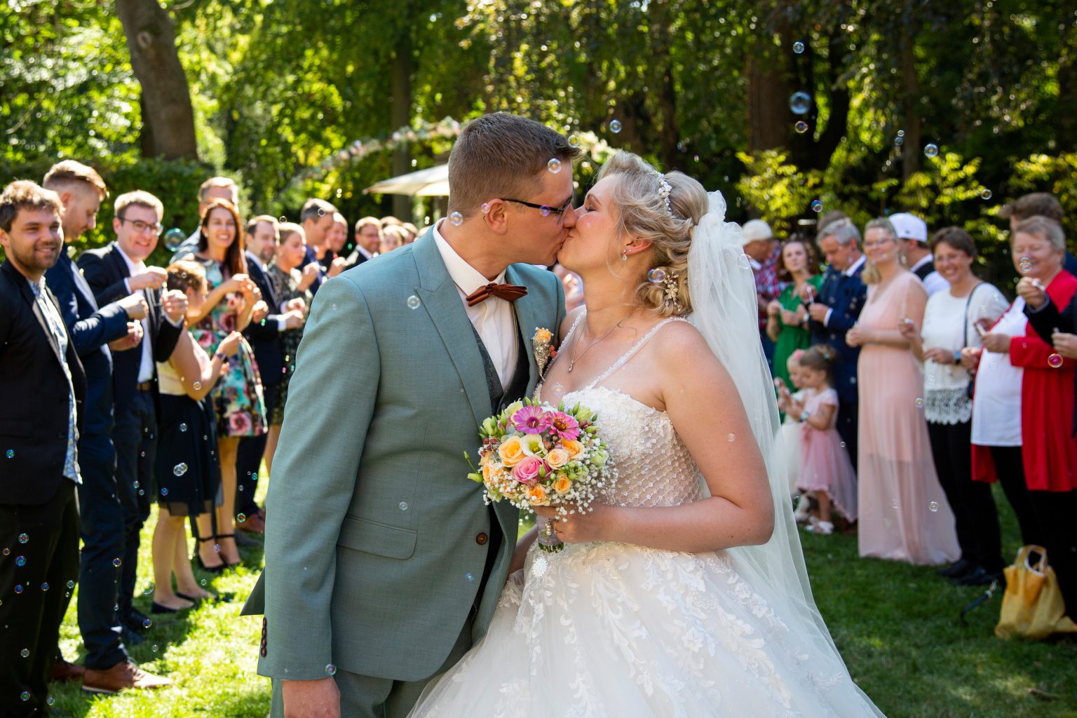 Hochzeit_Lisa_und_Nico-213 Ein Hochzeitspaar küsst sich vor Gästen und Sarah Seiler Fotografie hält diesen Moment fest.