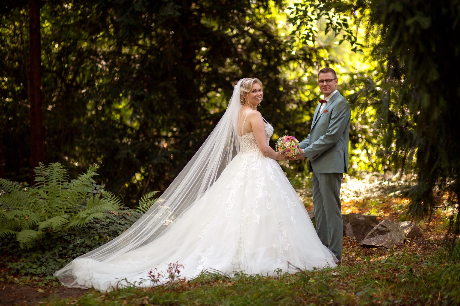 Hochzeitsfoto von Sarah Seiler Fotografie Ein Hochzeitspaar steht im Wald und Sarah Seiler Fotografie fotografiert sie.