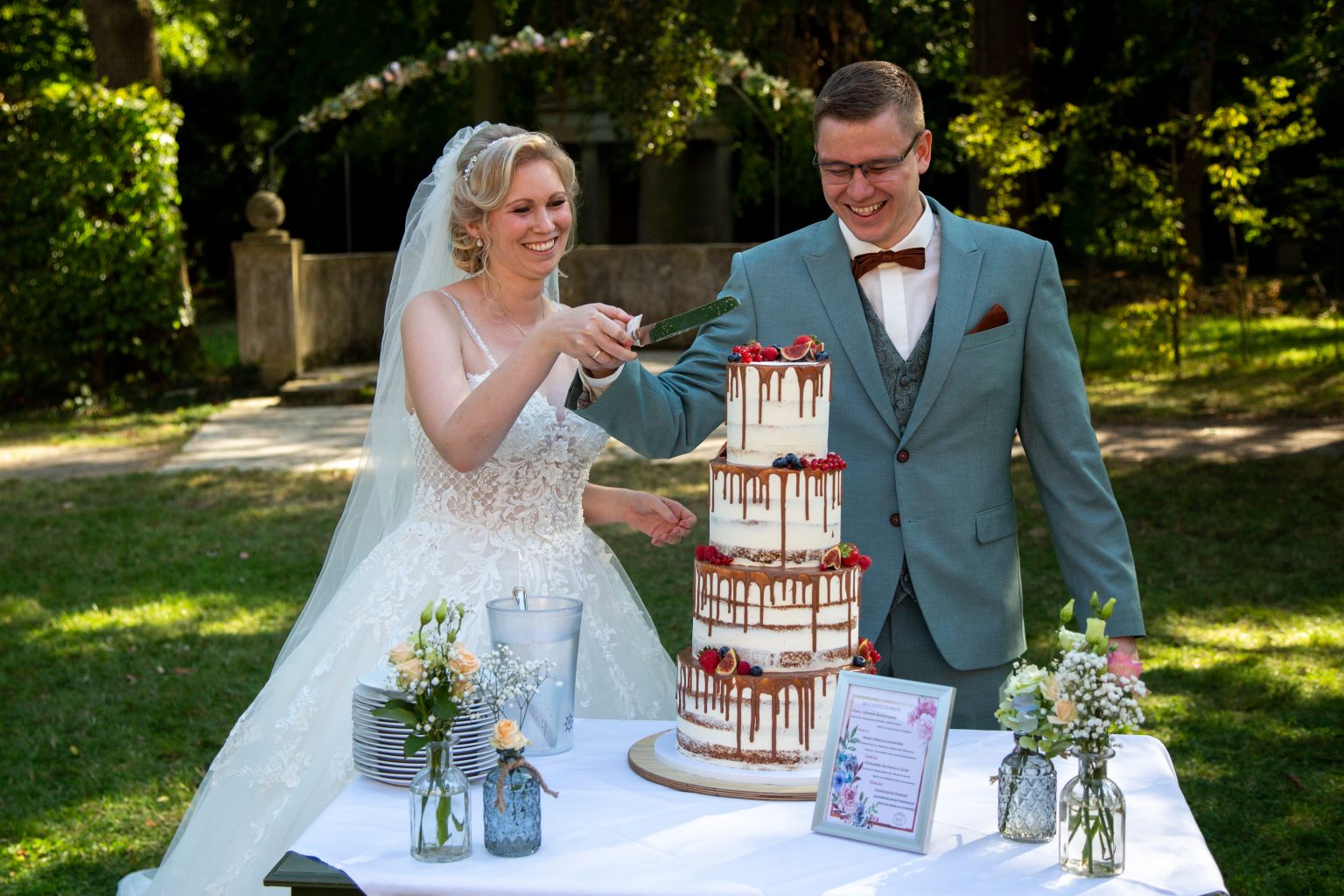 Hochzeitsfoto von Sarah Seiler Fotografie Ein Hochzeitspaar steht lächelnd am Tisch mit ihrer Hochzeitstorte und Sarah Seiler Fotografie hält diesen Moment fest.